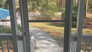 A wooden deck with a white door leading to a yard with a tree, a car, and a blue tarp.