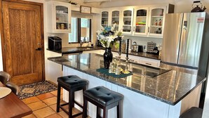 A kitchen with a central island, bar stools, a refrigerator, and various kitchen items. - Private Forest Lodge w/Game House, Spa, mins to DT (Prescott)