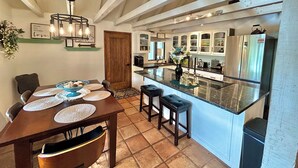 A kitchen with a central island, wooden beams, and a dining area with a table set for four. - Private Forest Lodge w/Game House, Spa, mins to DT (Prescott)