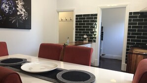 A dining area with a white table, red chairs, and black and gray placemats. - Poppy’s Place, a beautiful family & pet friendly1920’s bungalow.  (Angaston)