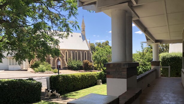 A covered outdoor area with a stone column, a grassy lawn, and a church in the background. - Poppy’s Place, a beautiful family & pet friendly1920’s bungalow.  (Angaston)