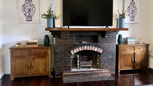 A living room with a brick fireplace, wooden cabinets, a mounted TV, and decorative vases. - Poppy’s Place, a beautiful family & pet friendly1920’s bungalow.  (Angaston)