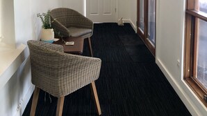 A narrow hallway with a dark carpet, a wicker chair, a small table with a plant, and a door with frosted glass panels. - Poppy’s Place, a beautiful family & pet friendly1920’s bungalow.  (Angaston)