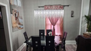 A dining area with a table and chairs, a chandelier, and a window with curtains. - High Ceilings | King Beds | 85” TV | Near Downtown (Winston-Salem)
