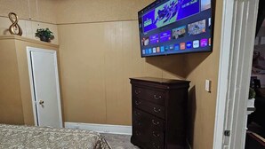 A bedroom with a bed, a dresser, a TV mounted on the wall, a ceiling fan, and a door. - High Ceilings | King Beds | 85” TV | Near Downtown (Winston-Salem)