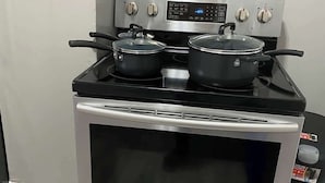 A stainless steel oven with a digital control panel, two pots on the stove, and a trash bin to the right. - High Ceilings | King Beds | 85” TV | Near Downtown (Winston-Salem)