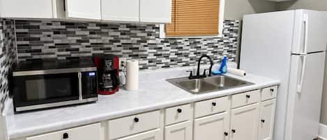 A kitchen with white cabinets, a microwave, a sink, and a refrigerator.