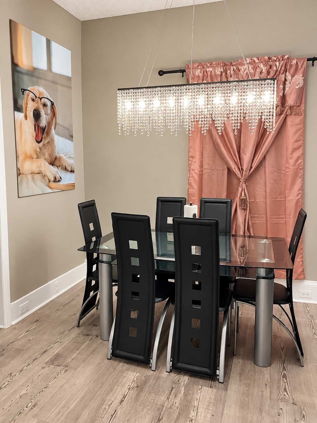 A dining area with a glass table, black chairs, a chandelier, and a framed picture on the wall.