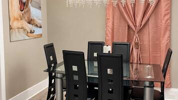 A dining area with a glass table, black chairs, a chandelier, and a framed picture on the wall.