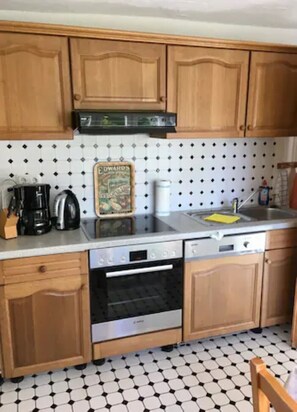 Una cocina con armarios de madera, salpicadero de azulejos, cafetera, tostadora y lavavajillas.