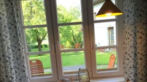 Un coin repas avec une table dressée pour deux personnes, un vase rempli de fleurs et une vue sur un jardin, visible à travers de grandes fenêtres.