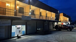 Un edificio de varios pisos, un cartel que indica 'Soon to OPEN... PAANAKAN' y un coche estacionado adelante.