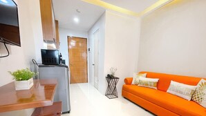 Un espacio habitable compacto con kitchenette, zona de comedor y sofá naranja brillante.