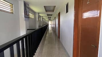 A long, narrow hallway with a marble floor, wooden doors, and a black railing.