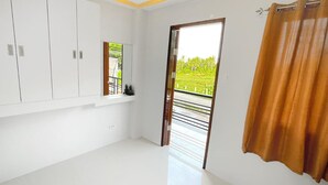 Una habitación con paredes blancas, un armario grande, un espejo, una ventana con vistas a zonas verdes y una cortina.