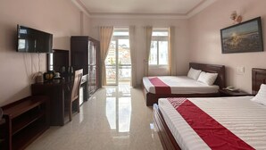 Habitación de hotel con dos camas, televisión, escritorio y balcón con vistas a edificios.