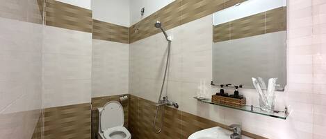 A bathroom with a toilet, a sink, a shower, and a mirror.