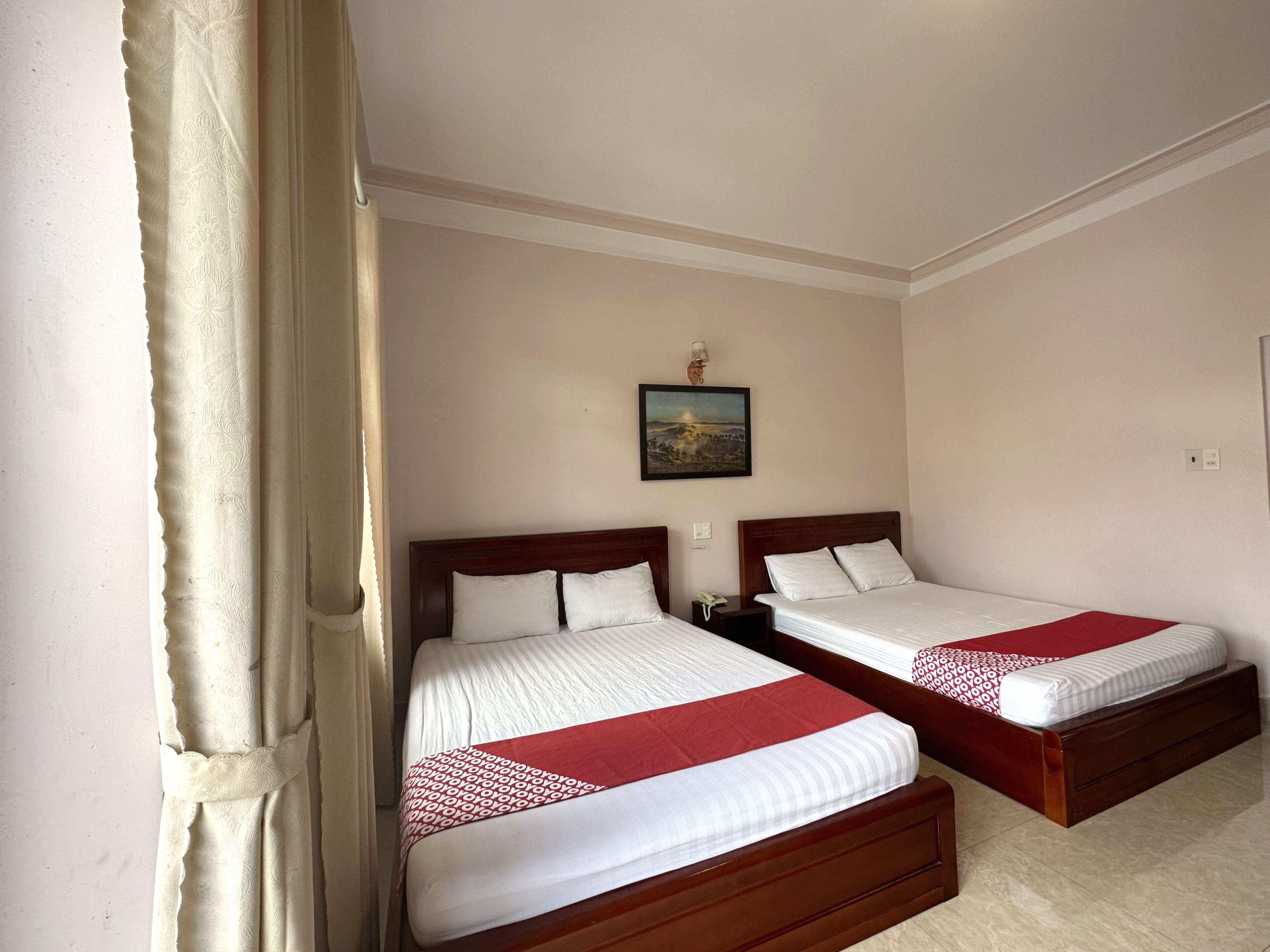 A hotel room with two beds, a painting on the wall, and a curtain on the left.