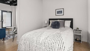 Een slaapkamer met een bed, nachtkastje, lamp, fotokader en stoel.