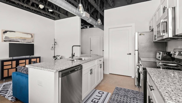 Een moderne keuken met witte kastjes, een RVS vaatwasser en een inbouwoven. Op de vloer ligt een zwart-wit tapijt met een patroon.