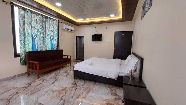 A bedroom with a bed, a wooden bench, a TV, and a wardrobe. - Samriddhi Hotel Banquet and Lawn (Varanasi)