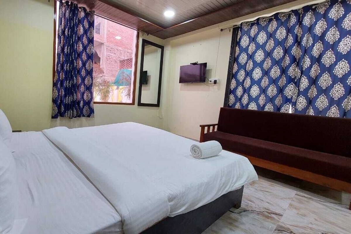 A bedroom with a bed, a bench, a TV, and curtains.