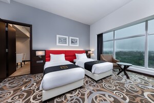 Una habitación de hotel con dos camas, un cabecero rojo, un ventanal grande y suelo alfombrado.