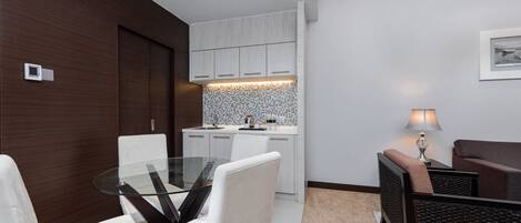 A modern kitchen with white cabinets, a glass dining table, and a small seating area with a lamp.
