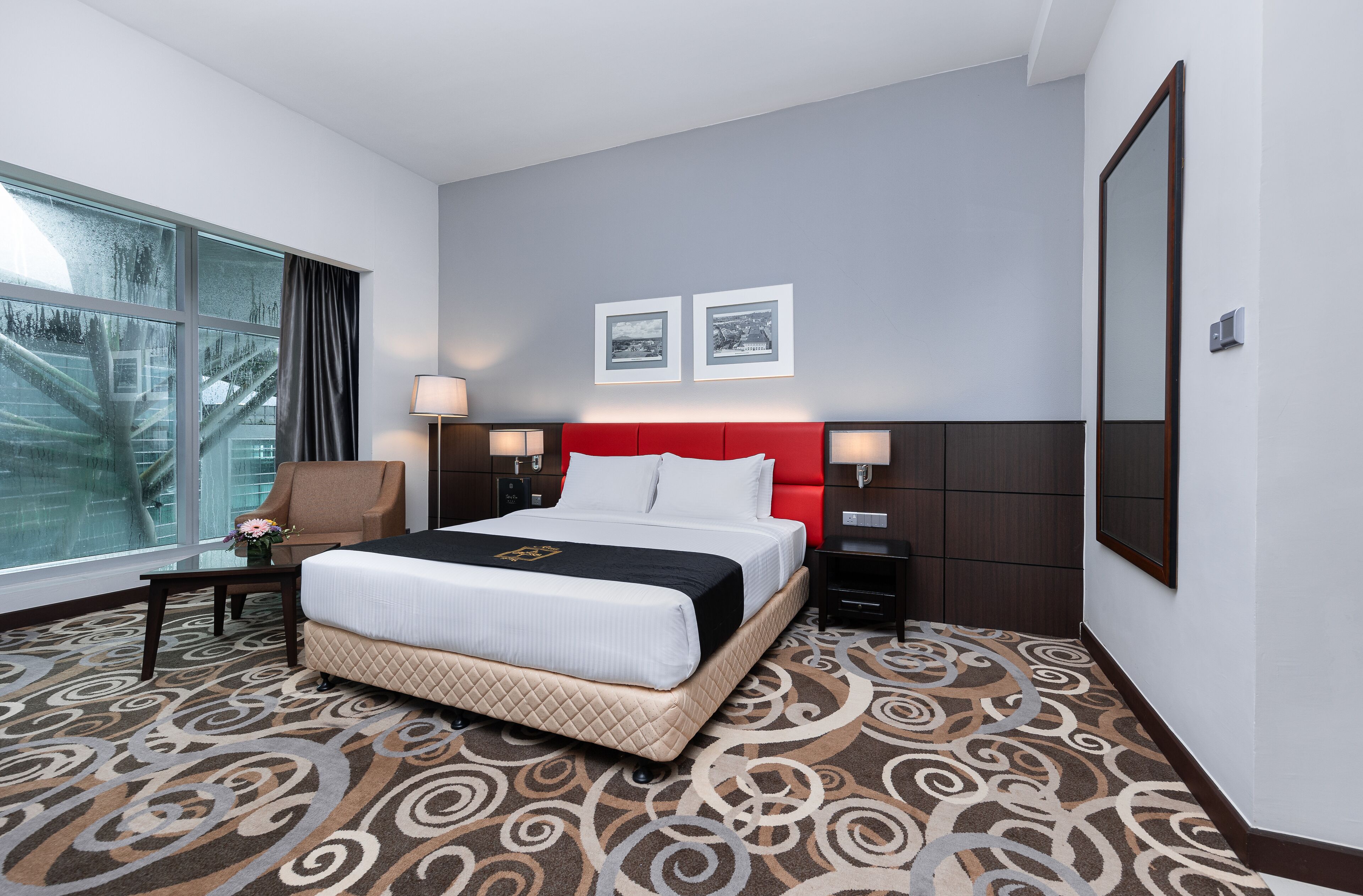 Una habitación de hotel con una cama grande, dos mesitas de noche, una silla y un ventanal con cortinas.