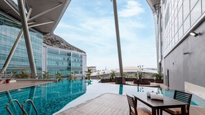 A modern indoor pool area with a glass wall, a pool table, and lounge chairs. - Raia Hotel & Convention Centre Kuching (Kuching)
