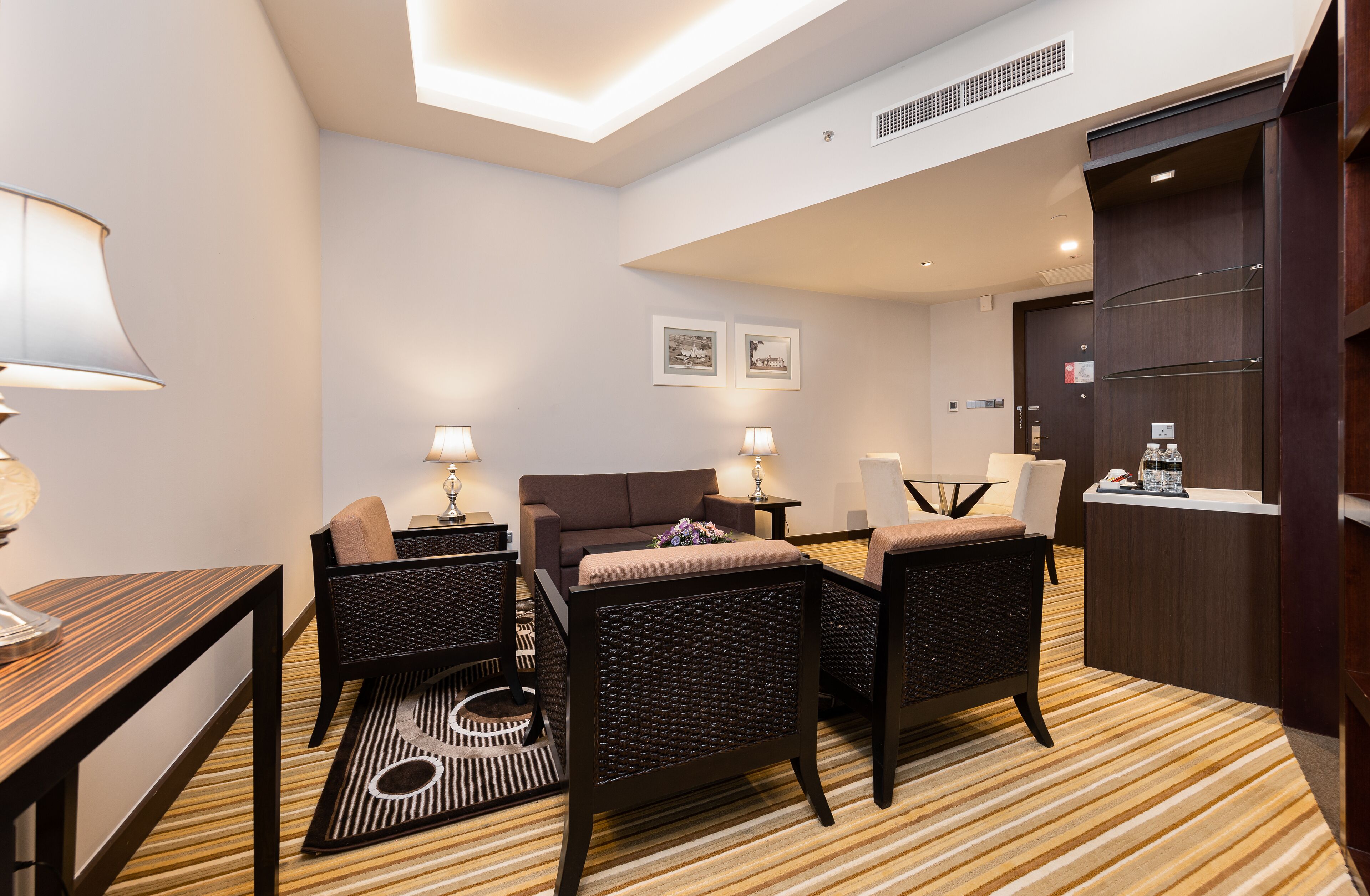 A hotel room with a sofa, two armchairs, a small table, a lamp, a coffee machine, and a minibar.