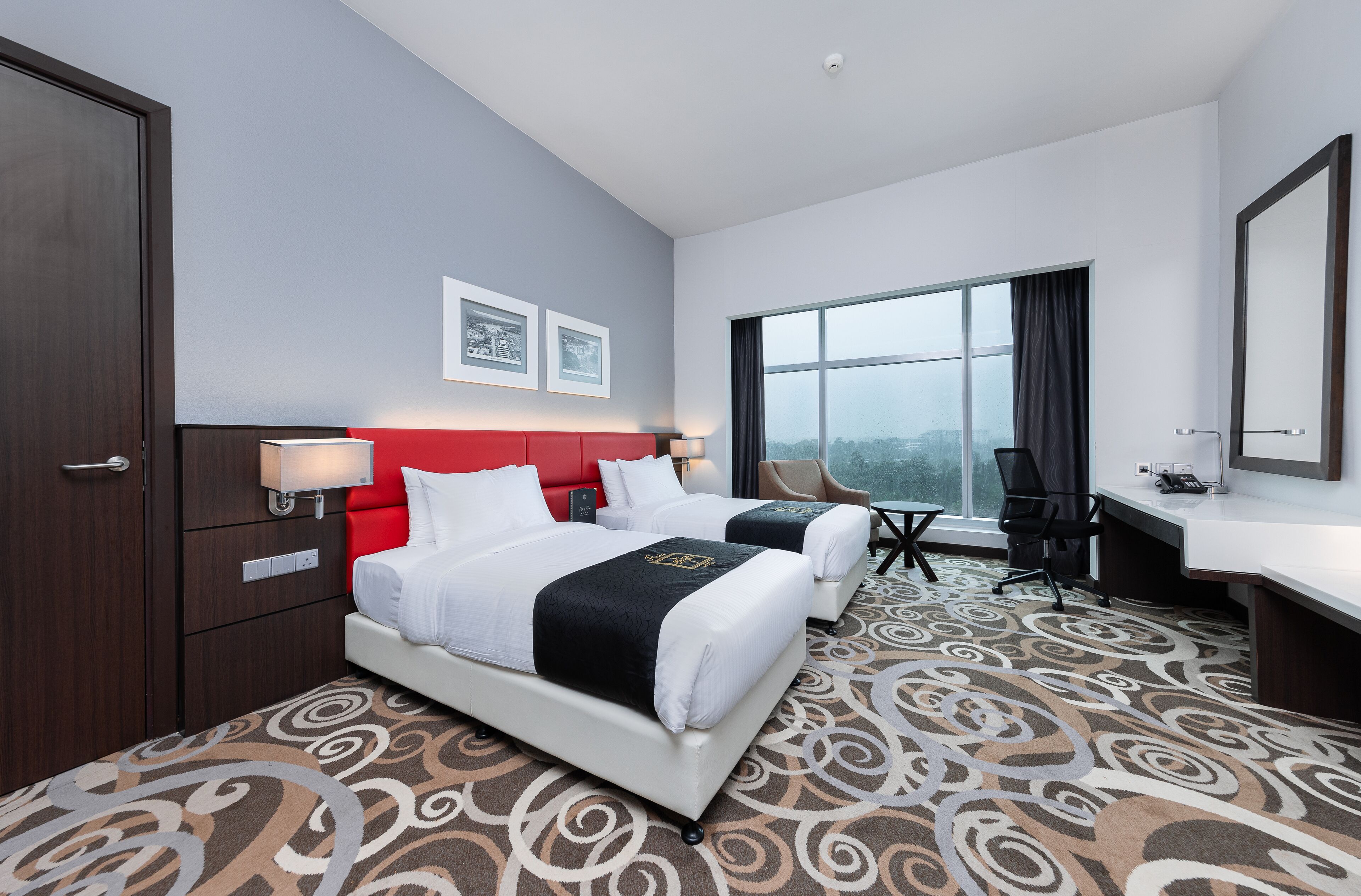 A hotel room with two beds, a desk, a chair, and a large window.