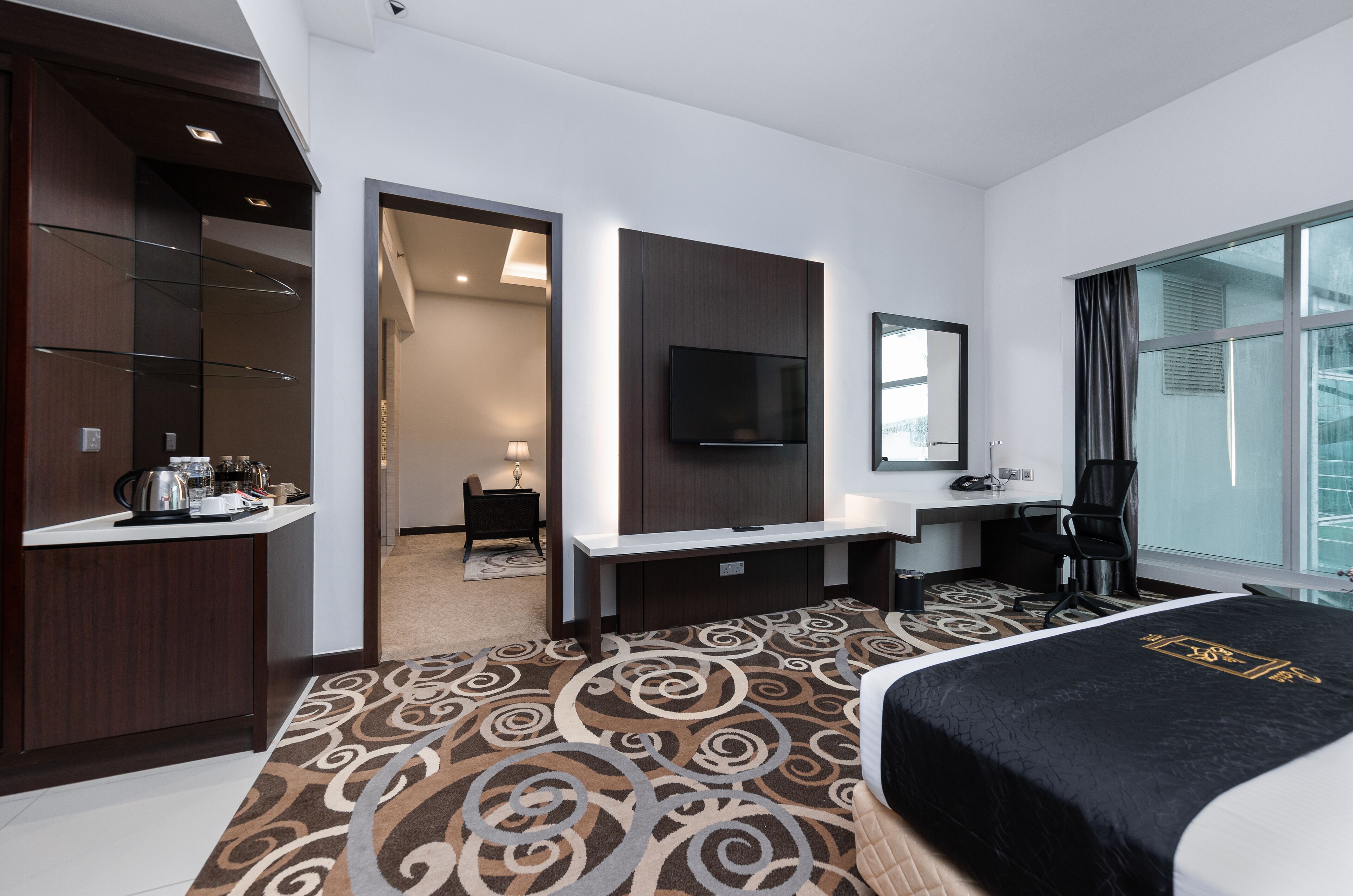 A hotel room with a large bed, a TV mounted on the wall, a desk with a chair, and a view through a window.