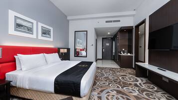 A hotel room with a red headboard, a large bed, a TV, a mirror, and a bathroom visible through an open door.