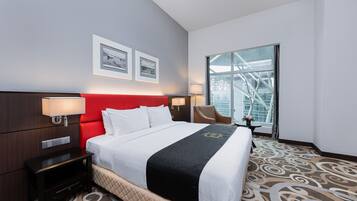 A hotel room with a large bed, a red headboard, two framed pictures on the wall, a window with a view of a building, and a carpet with a swirl pattern.