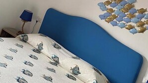 A bedroom with a blue headboard, a bed with a fish pattern bedspread, a hanging lamp with star designs, and wall art of fish and starburst shapes. - The Rooms by the Sea (Portoferraio)