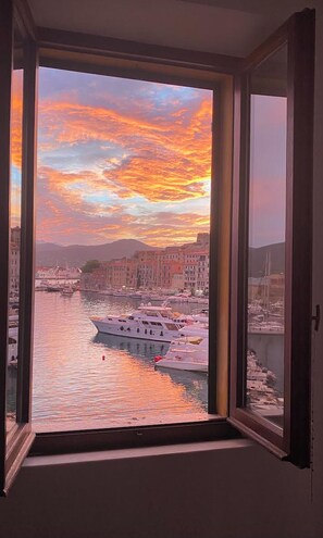 Vista desde una ventana hacia un puerto deportivo con barcos y edificios al atardecer.