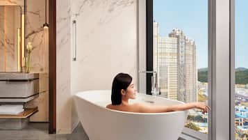 Un baño moderno con una bañera independiente, un revestimiento de mármol y un amplio ventanal con vistas a la ciudad.