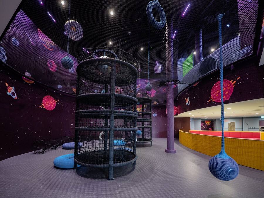 Zona de juegos con una estructura de red, un objeto esférico colgante y un mostrador con una decoración en rojo y amarillo.
