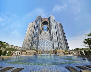 A modern hotel with a distinctive circular skylight and a large swimming pool in the foreground. - Epic Tower - Studio City Macau (Cotai)