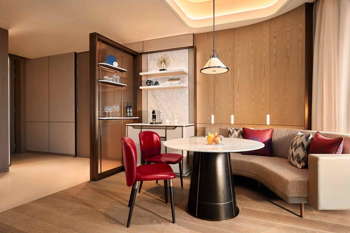 A modern living room with a round table, red chairs, a sofa with patterned cushions, and built-in wooden cabinets.