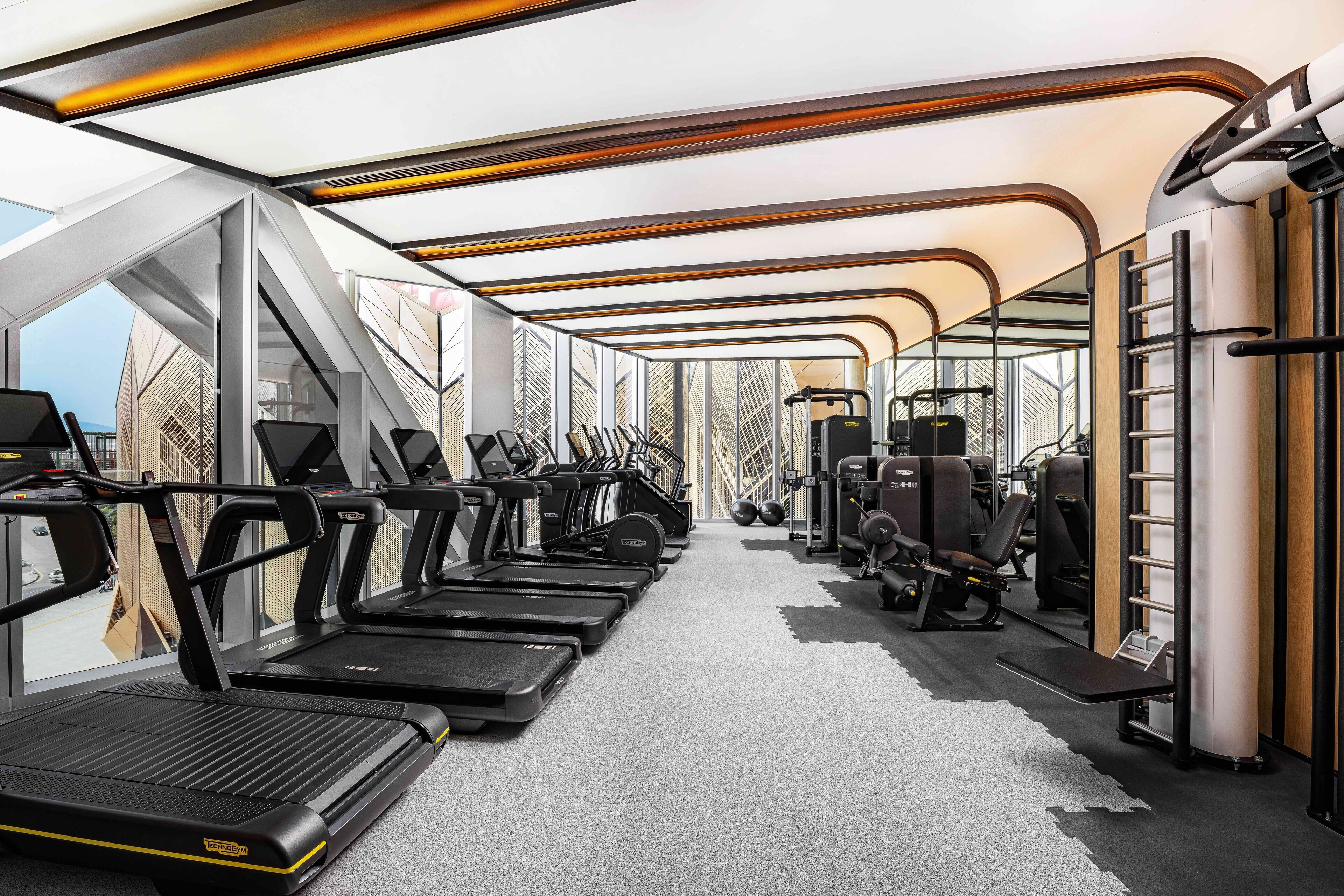 Un gimnasio moderno con cintas de correr, máquinas de pesas y un amplio ventanal con vistas a la ciudad.