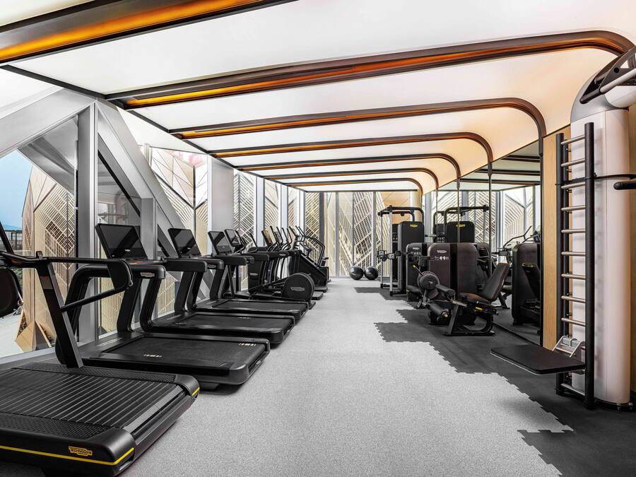 Un gimnasio moderno con cintas de correr, máquinas de pesas y un amplio ventanal con vistas a la ciudad.