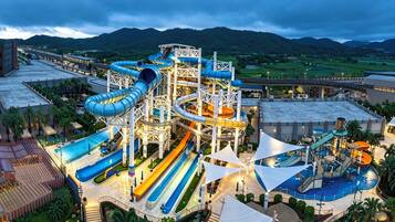 Een waterpark met meerdere glijbanen en zwembaden, omgeven door groen en heuvels.