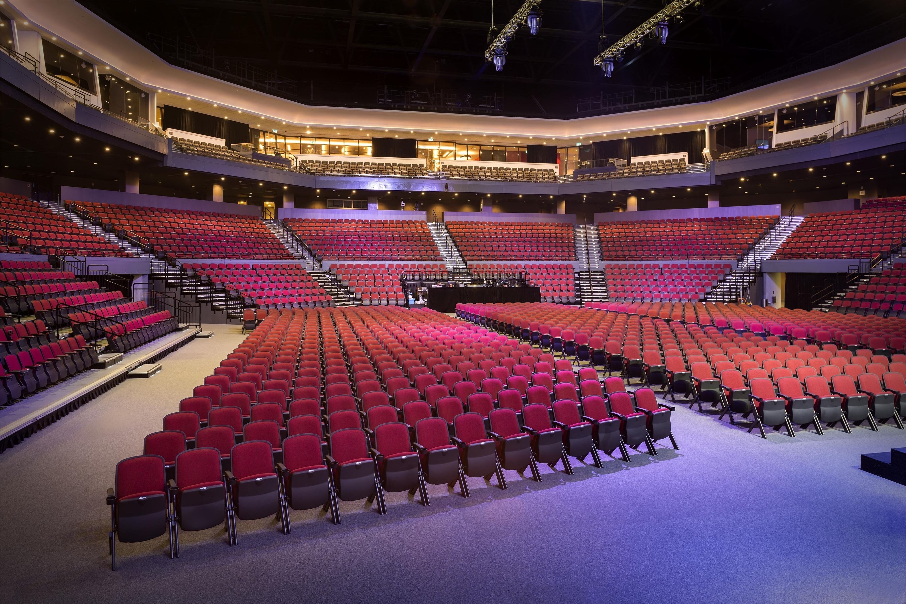 A large, multi-tiered auditorium with red seating and a central stage.