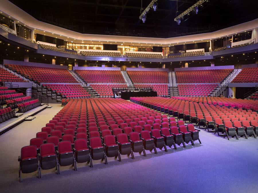 A large, multi-tiered auditorium with red seating and a central stage.