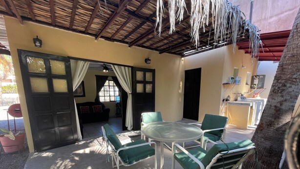 An outdoor patio with a round table and green chairs, a ceiling fan, and a view of the interior through a doorway. - Casa arroyo at Bajazul just steps of waterfront and downtown (Loreto)