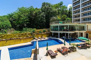 Um hotel com piscina na cobertura, espreguiçadeiras e um andar superior envidraçado.