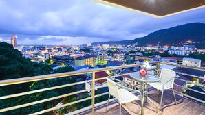 A balcony with a table and chairs, overlooking a cityscape with buildings and hills. - Beststayinphuket Poolview (Patong)