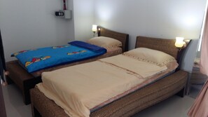 Quarto duplo com duas camas de solteiro, mesa de cabeceira com abajur, aquecedor fixado na parede e tomada.
